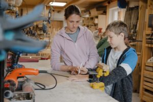 Bild von einer Frau und einem Jungen die bei einer Werkbank stehen und mit einem Bleistift Holz markieren