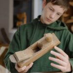 Ein Junge der einen alten Holzhobel in der Hand hält und betrachtet