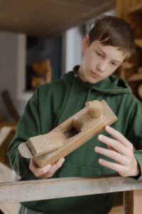 Ein Junge der einen alten Holzhobel in der Hand hält und betrachtet